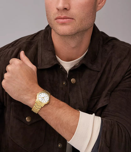 Reloj Fossil Heritage ME3226 automático dorado, lucido en muñeca de hombre, chaqueta marrón y camiseta clara.