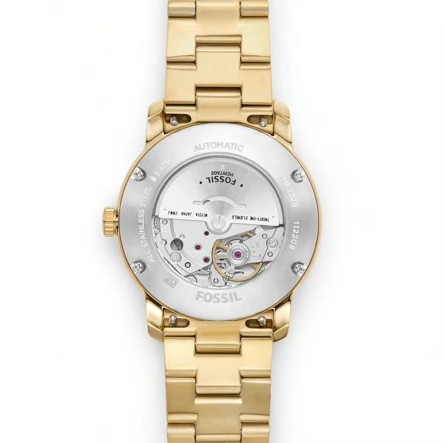 Vista trasera reloj Fossil Heritage ME3226 automático, caja dorada, maquinaria visible, detalles de acero y fondo blanco.