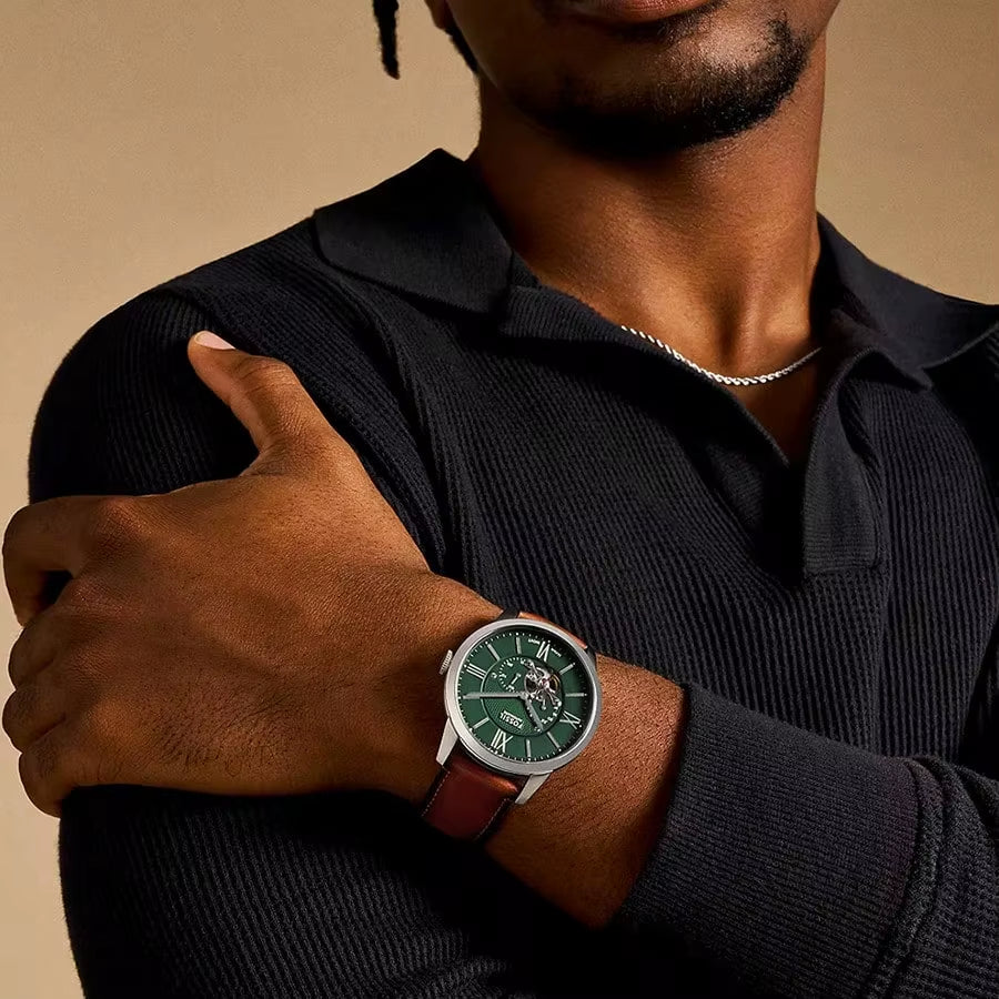 Reloj Fossil ME3265 automático con esfera verde y correa marrón, puesto en la muñeca de un hombre vestido de negro, vista frontal.