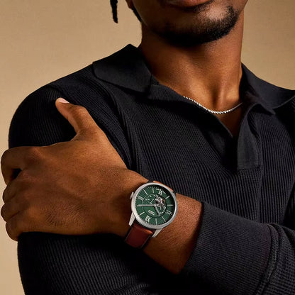 Reloj Fossil ME3265 automático con esfera verde y correa marrón, puesto en la muñeca de un hombre vestido de negro, vista frontal.