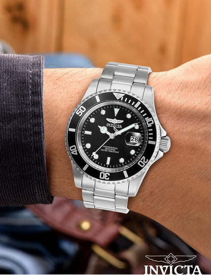 Reloj Invicta Pro Diver 26970, acero con bisel y esfera negra, lucido en la muñeca, camisa oscura y fondo cálido.