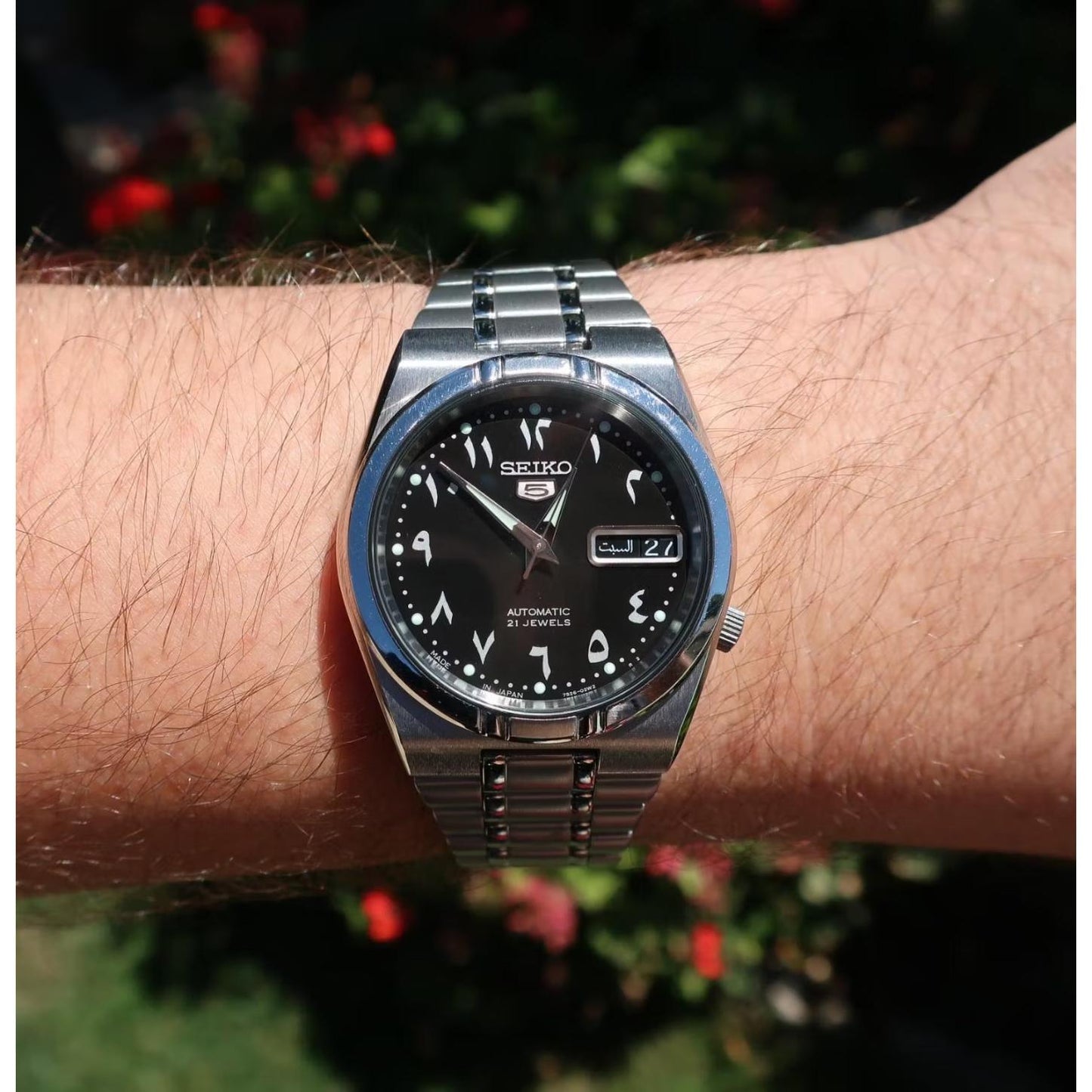 Seiko 5 SNK063J5 automatic watch worn on the wrist, featuring a black Arabic numeral dial, day-date display, luminous markers, and stainless steel bracelet.