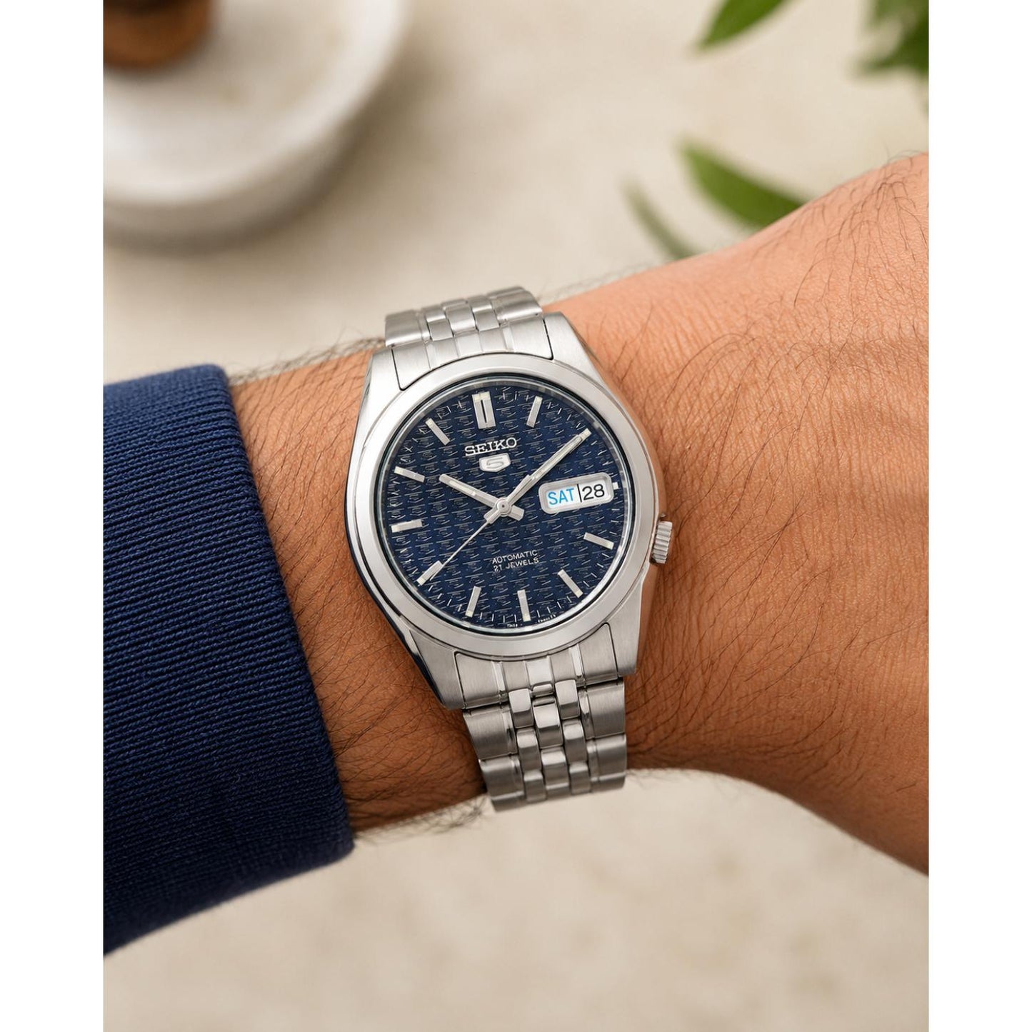 Seiko 5 SNK357K1 automatic watch worn on the wrist, featuring a textured blue dial, silver-tone hour markers, day-date display, and stainless steel bracelet.