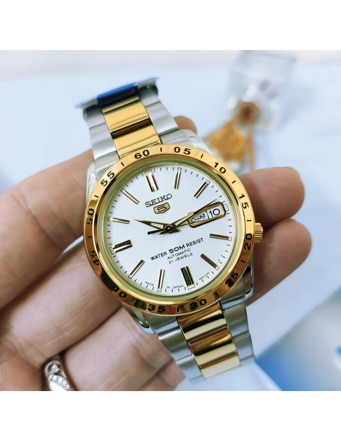reloj Seiko con brazalete de acero bicolor, esfera blanca con índices dorados y ventana de día y fecha, sostenido en la mano