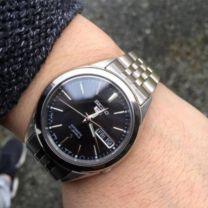 Seiko 5 SNKL23J1 automatic timepiece with a black dial and multi-link stainless steel bracelet displayed on wrist
