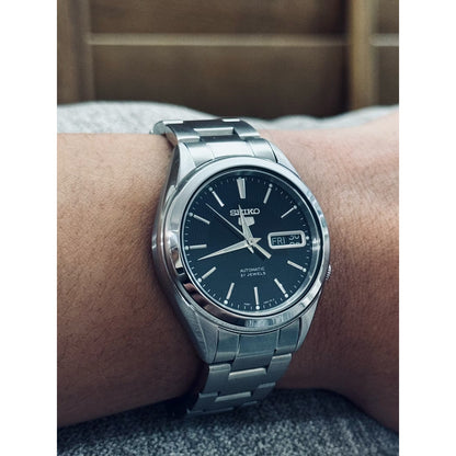 Seiko 5 SNKL23J1 men's automatic watch featuring a textured black dial and stainless steel bracelet worn on the wrist