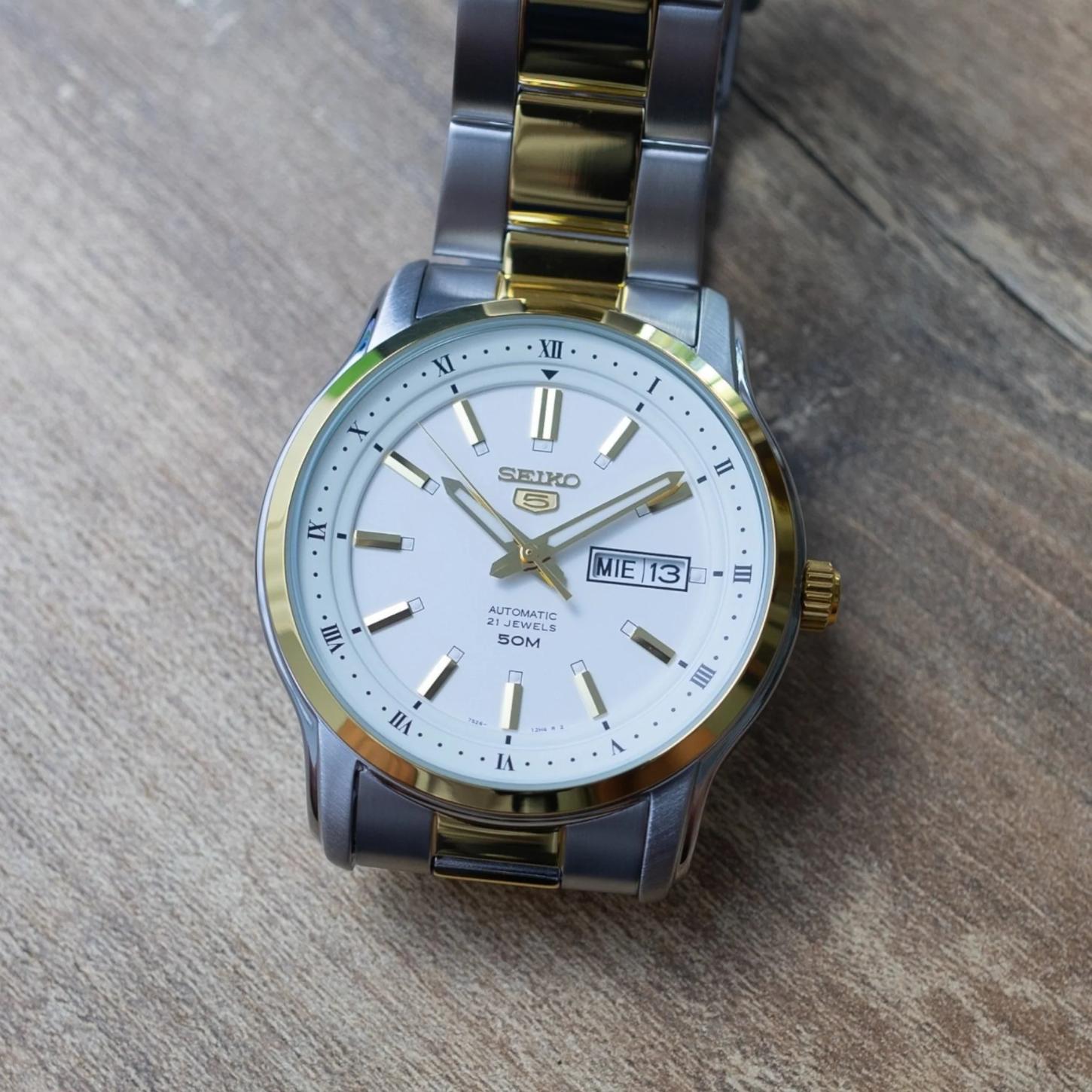 Seiko 5 SNKP14K1 automatic dress watch with white dial, gold-tone accents, day-date display and two-tone stainless steel bracelet in lifestyle setting.