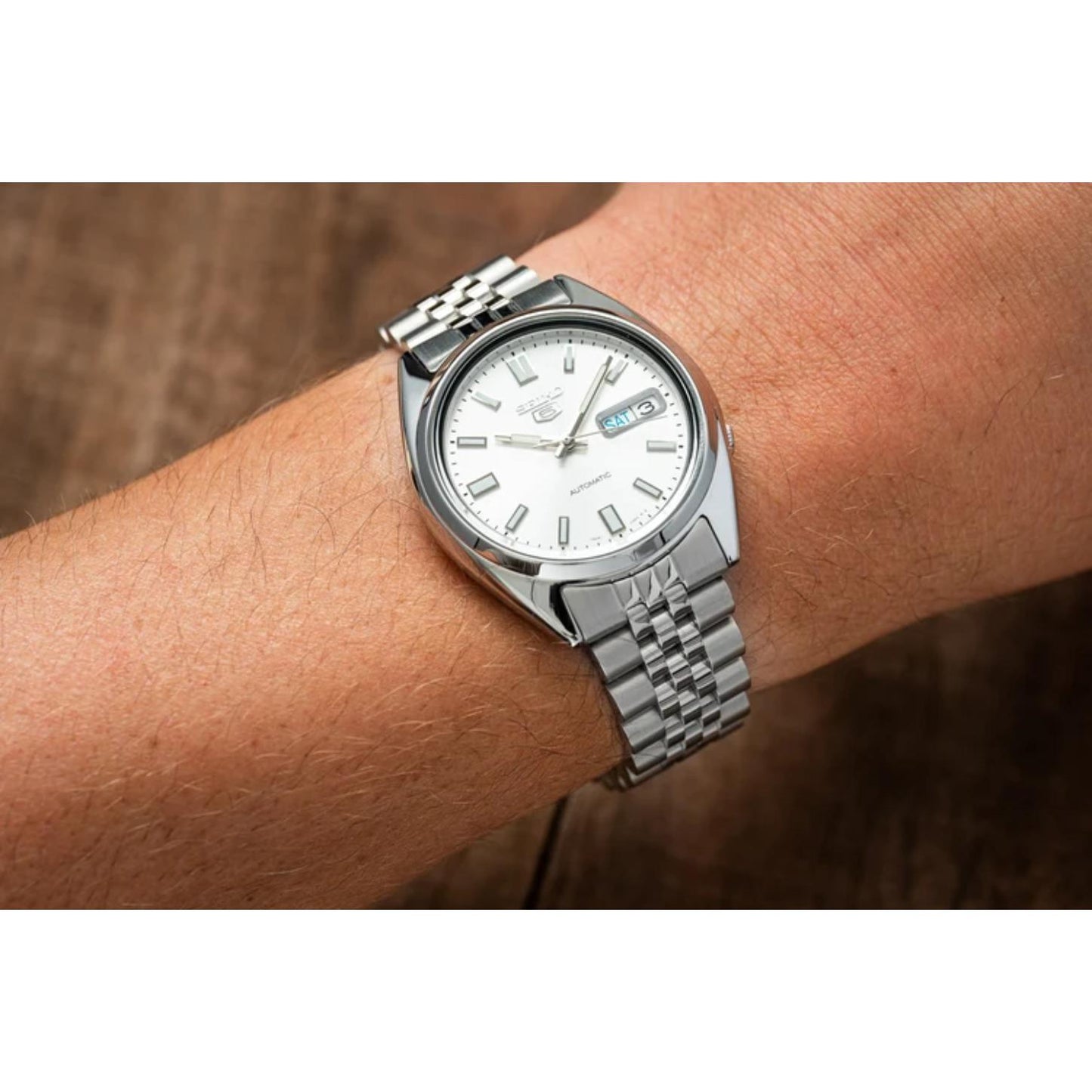 Seiko 5 SNXS73K1 automatic watch worn on the wrist, featuring a silver dial, day-date display, luminous hour markers, polished case, and stainless steel bracelet.