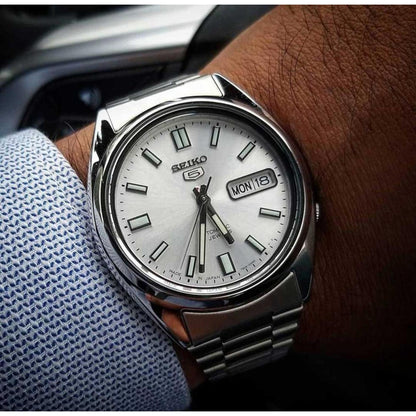 Seiko 5 SNXS73K1 automatic watch worn on the wrist, featuring a silver dial, luminous hour markers, day-date display, polished silver-tone case, and stainless steel bracelet.