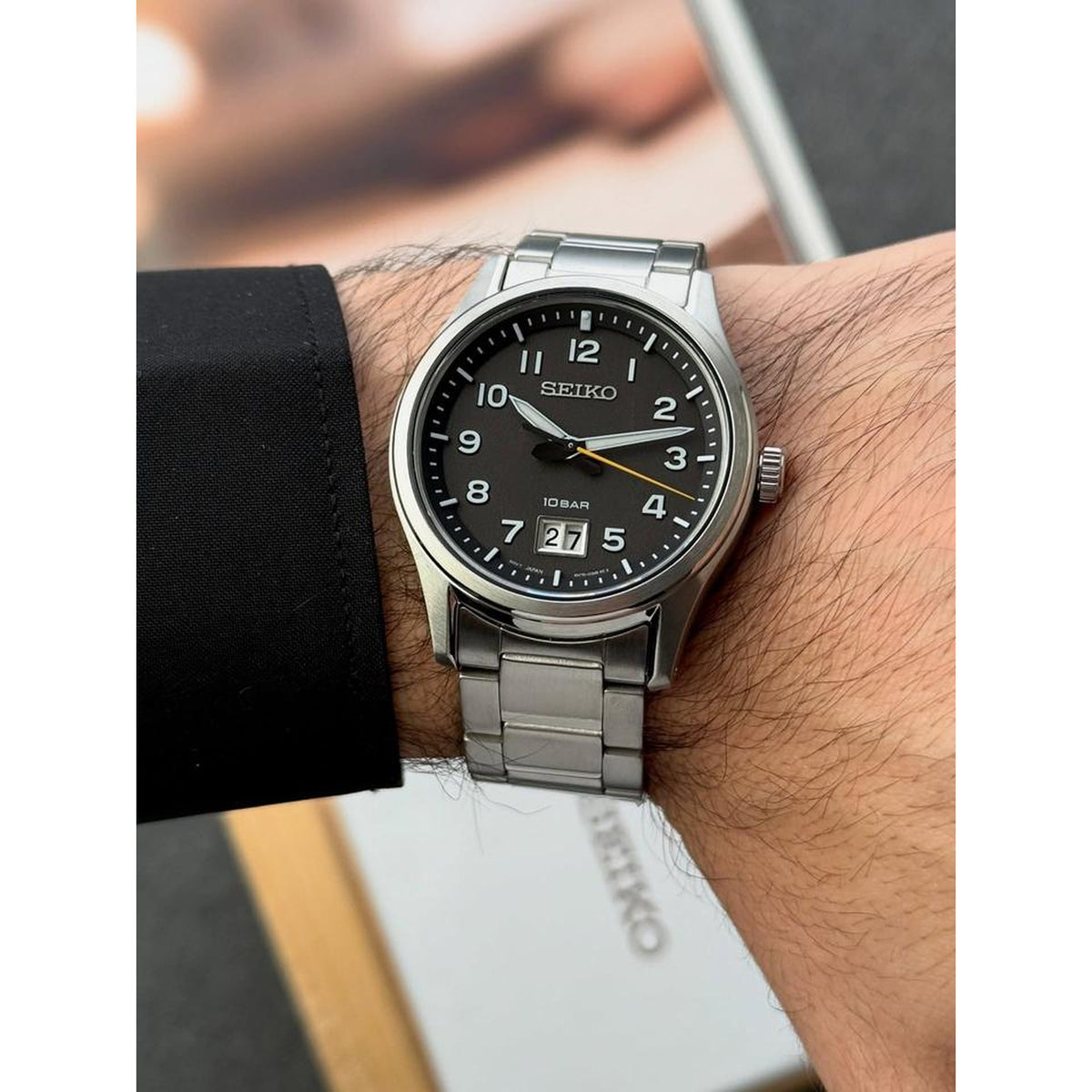 Seiko Classic SUR569P1 men's quartz watch with black dial and stainless steel bracelet shown on a wrist.