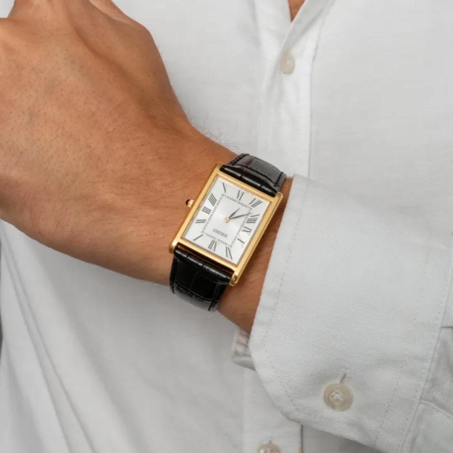 Seiko Classic SWR104P1 worn with a white shirt, featuring a rectangular gold-tone case, white Roman numeral dial, and black leather strap.