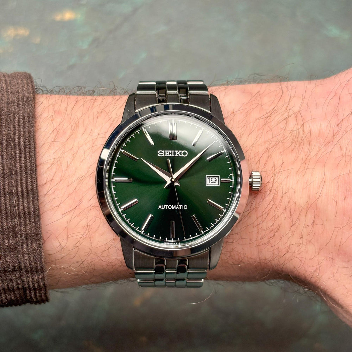 Close-up wrist shot of the Seiko Essentials SRPH89K1 automatic watch with its striking green dial and multi-link stainless steel bracelet.