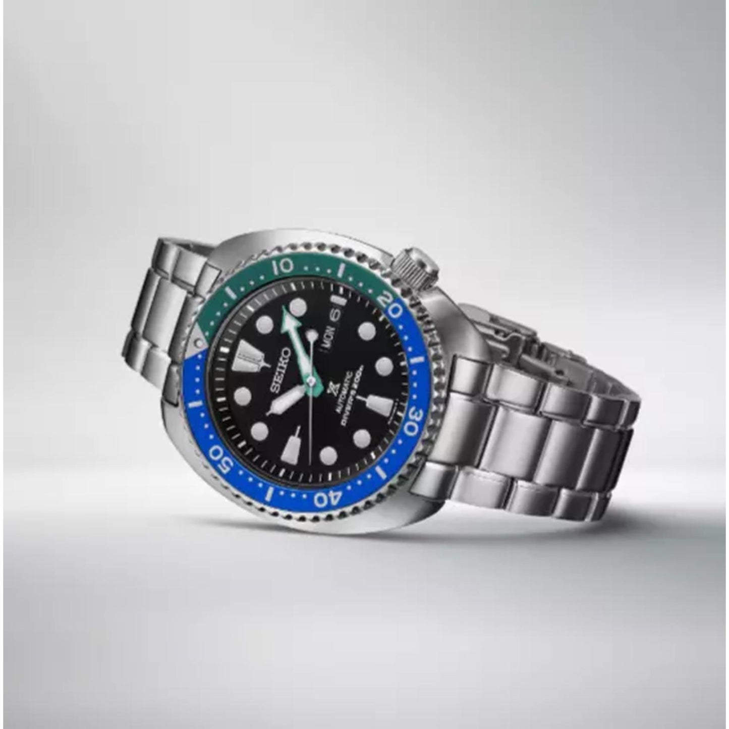 Seiko Prospex SRPJ35 automatic dive watch with black dial, Tropical Lagoon blue-green bezel and stainless steel bracelet displayed in minimalist lifestyle setting.
