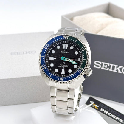 Seiko Prospex SRPJ35 automatic dive watch with black dial, Tropical Lagoon blue-green bezel and stainless steel bracelet displayed beside official Seiko Prospex packaging.