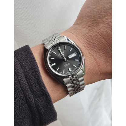 Seiko SNXS79K1 automatic watch worn on the wrist with black dial, day-date display and stainless steel bracelet.