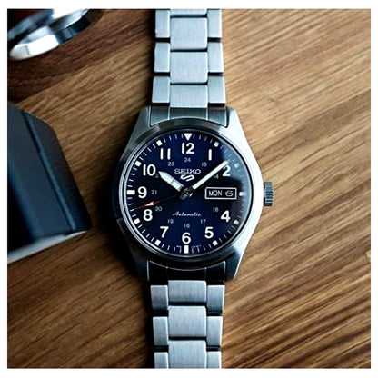 Seiko SRPG29K1 mens automatic field watch with blue dial and stainless steel bracelet displayed on wooden surface in lifestyle flat lay style