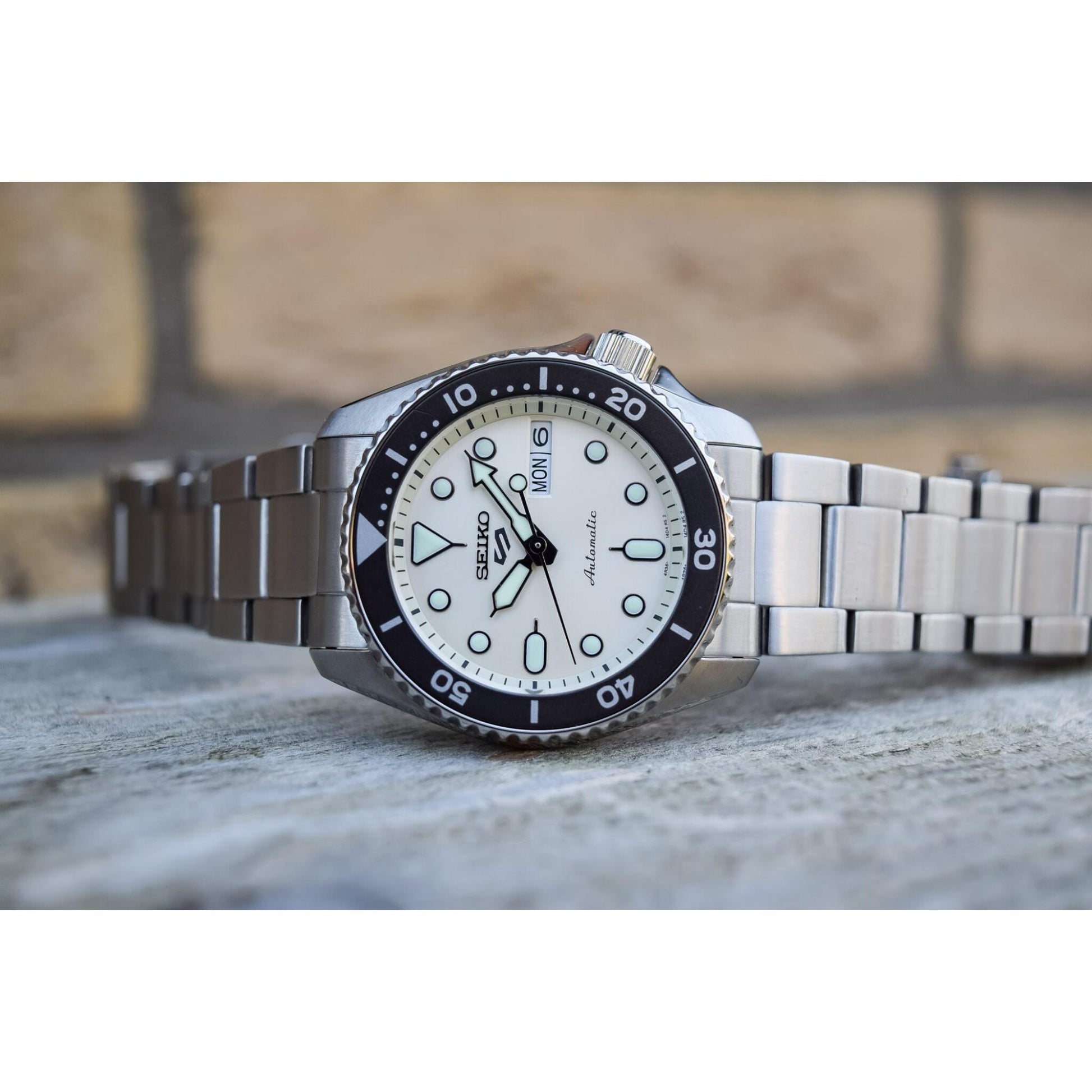 Seiko SRPK31 con esfera beige, bisel giratorio negro, índices luminiscentes, día y fecha a las 3 y brazalete de acero inoxidable.