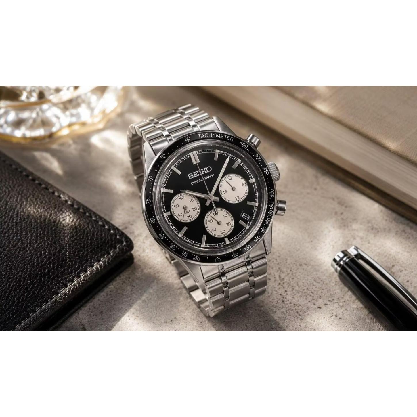 Seiko SSB479P1 chronograph displayed in a lifestyle setting, featuring a black reverse panda dial, three contrasting subdials, tachymeter bezel, and silver-tone bracelet.