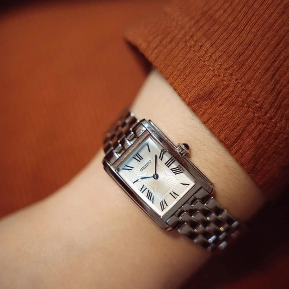 Seiko SWR083P1 women's quartz dress watch featuring a rectangular silver dial with Roman numerals and stainless steel bracelet worn on a wrist.