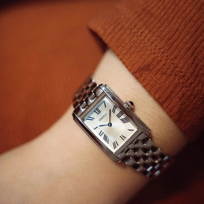 Seiko SWR083P1 women's quartz dress watch featuring a rectangular silver dial with Roman numerals and stainless steel bracelet worn on a wrist.