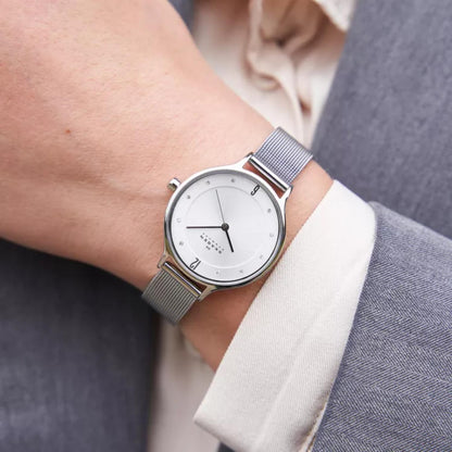 Skagen SKW2149 with white minimalist dial, crystal hour markers, polished silver-tone case, and stainless steel mesh bracelet worn on the wrist.
