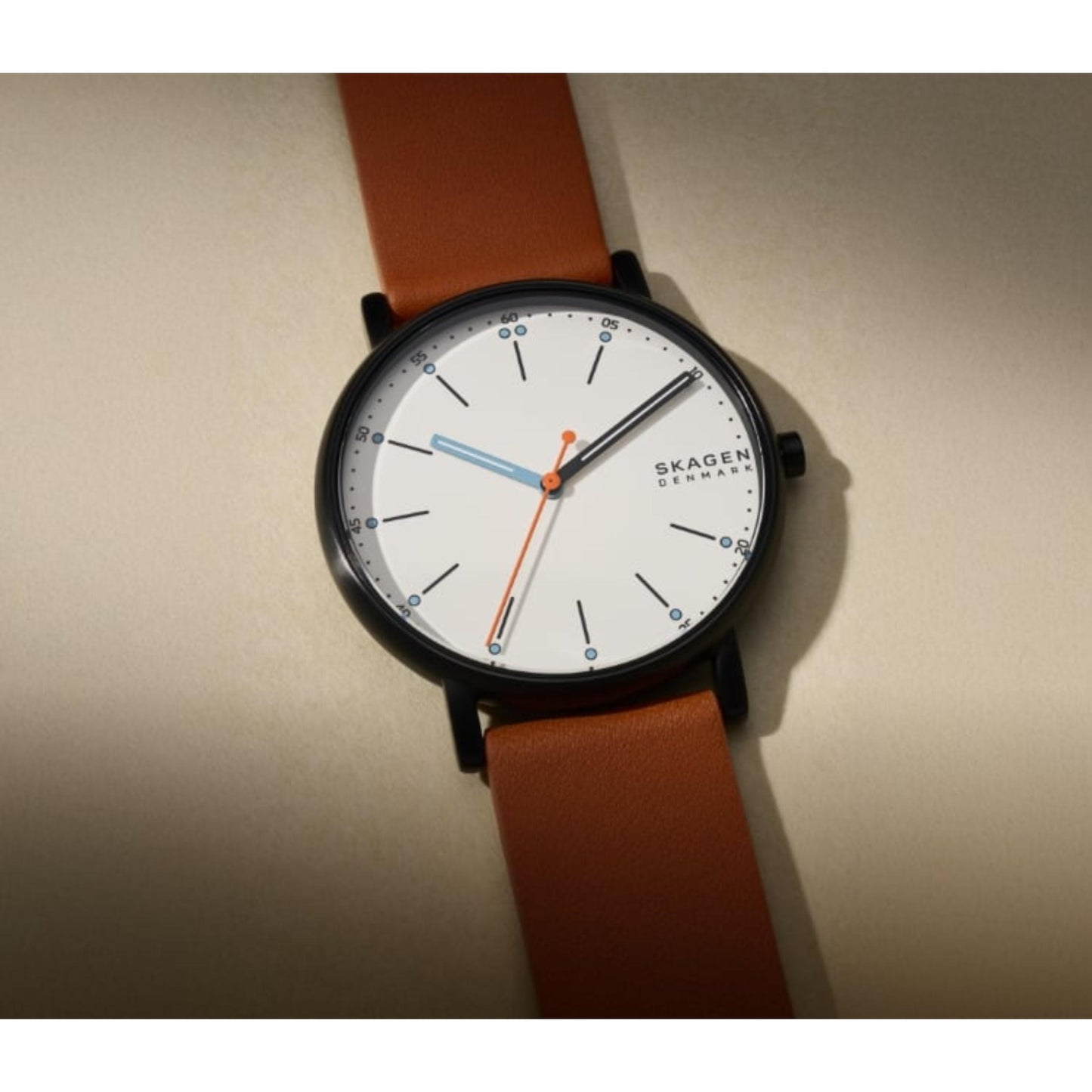 Skagen SKW6374 with white minimalist dial, gunmetal-tone case, orange seconds hand, and brown leather strap shown in a close-up angled view.