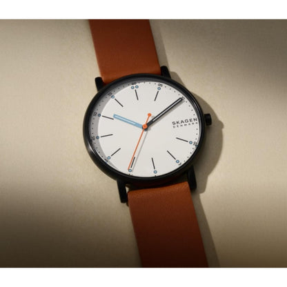 Skagen SKW6374 with white minimalist dial, gunmetal-tone case, orange seconds hand, and brown leather strap shown in a close-up angled view.
