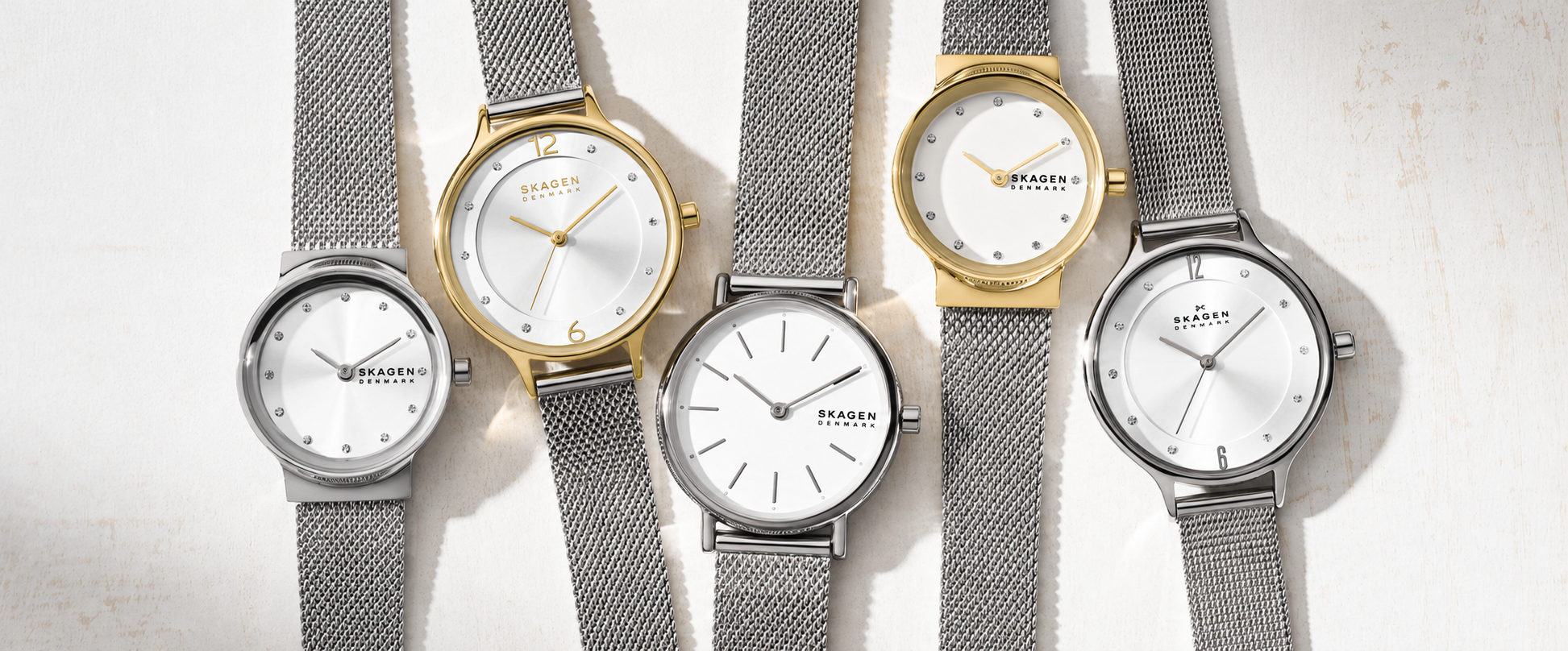 Skagen watches with white dials, silver-tone and gold-tone cases, minimalist hour markers, and stainless-style mesh bracelets arranged together.