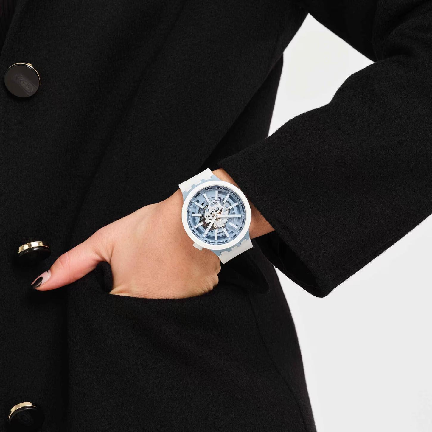 Swatch Big Bold Whice SB03N103 watch with a transparent blue openworked dial, white case, light blue accents, and white strap worn on the wrist.