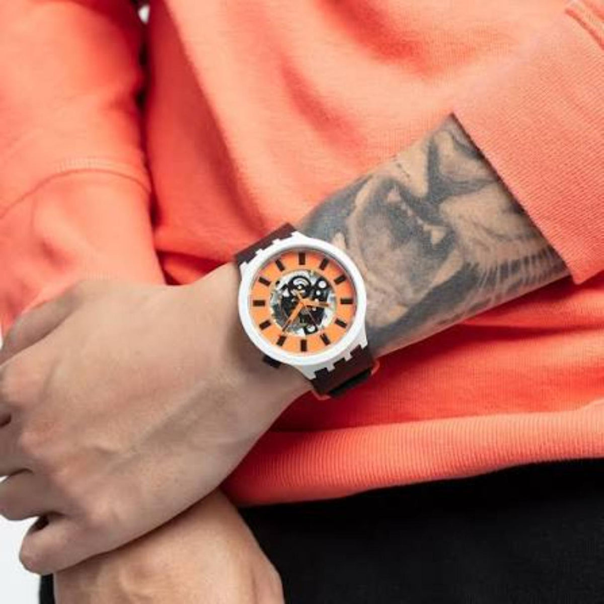 Swatch Bioceramic Orack SB03M104 watch with an orange skeleton dial, white case, black hour markers, and black strap worn on the wrist.