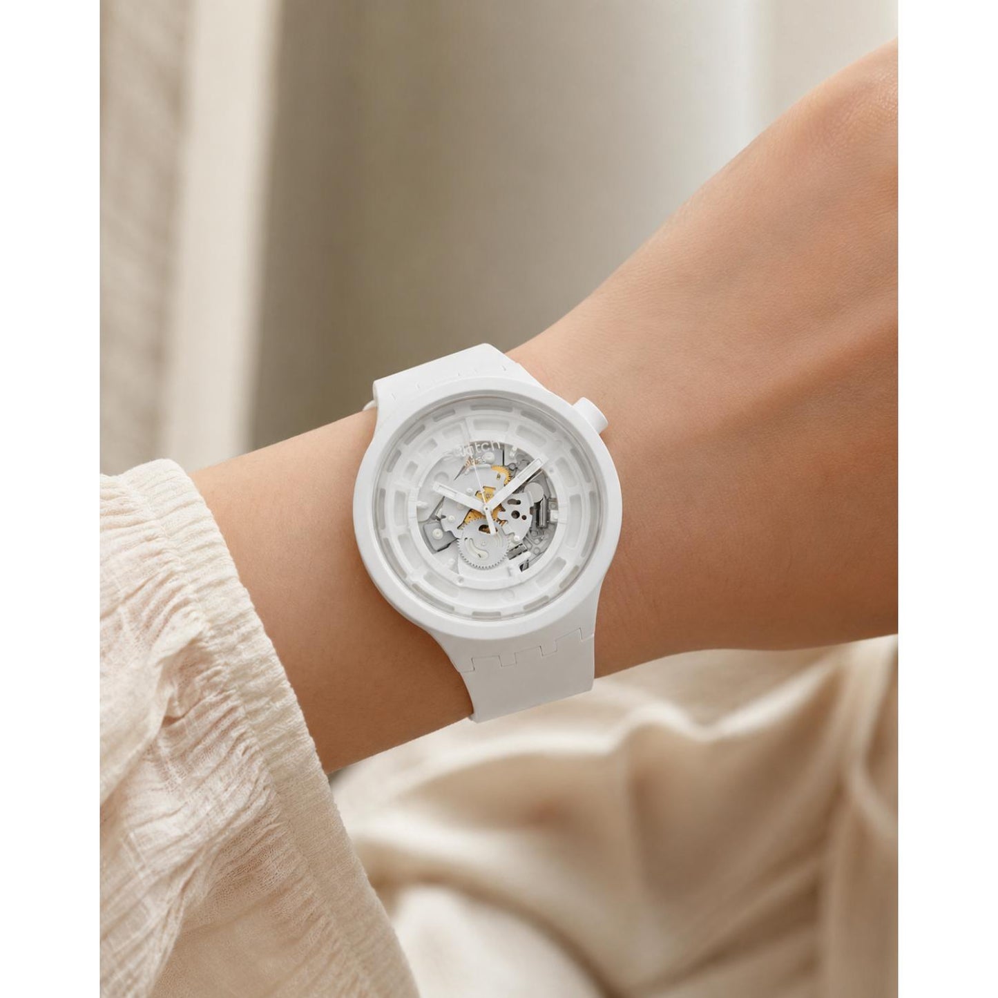 Swatch C-White SB03W100 oversized watch with a transparent openworked dial, white Bioceramic case, and matching white strap worn on the wrist.