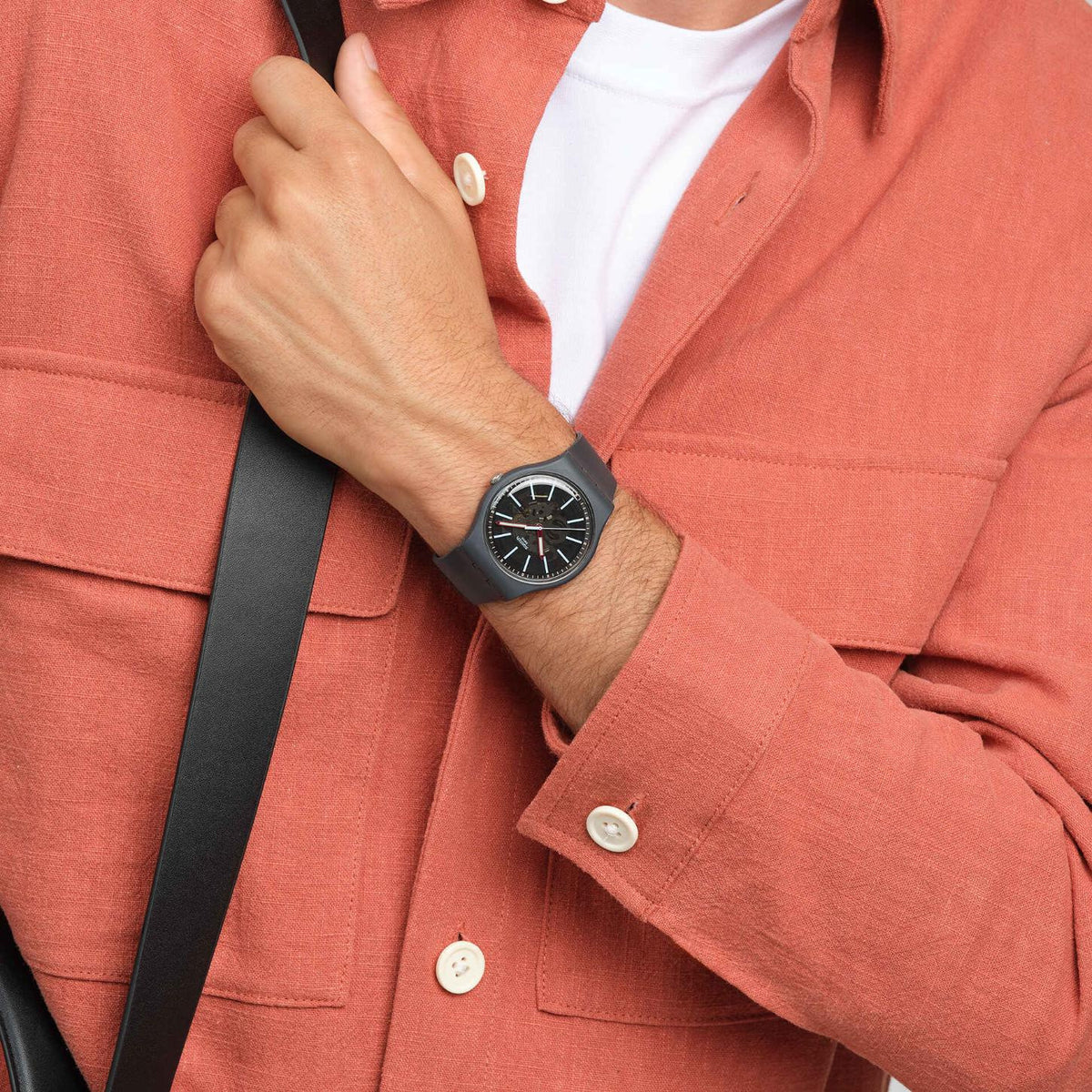 Swatch Cobblestone Street SO29A101 worn on the wrist with gray patterned dial, light blue hour markers, red hands, dark gray case, and matching dark gray strap in a casual outfit.