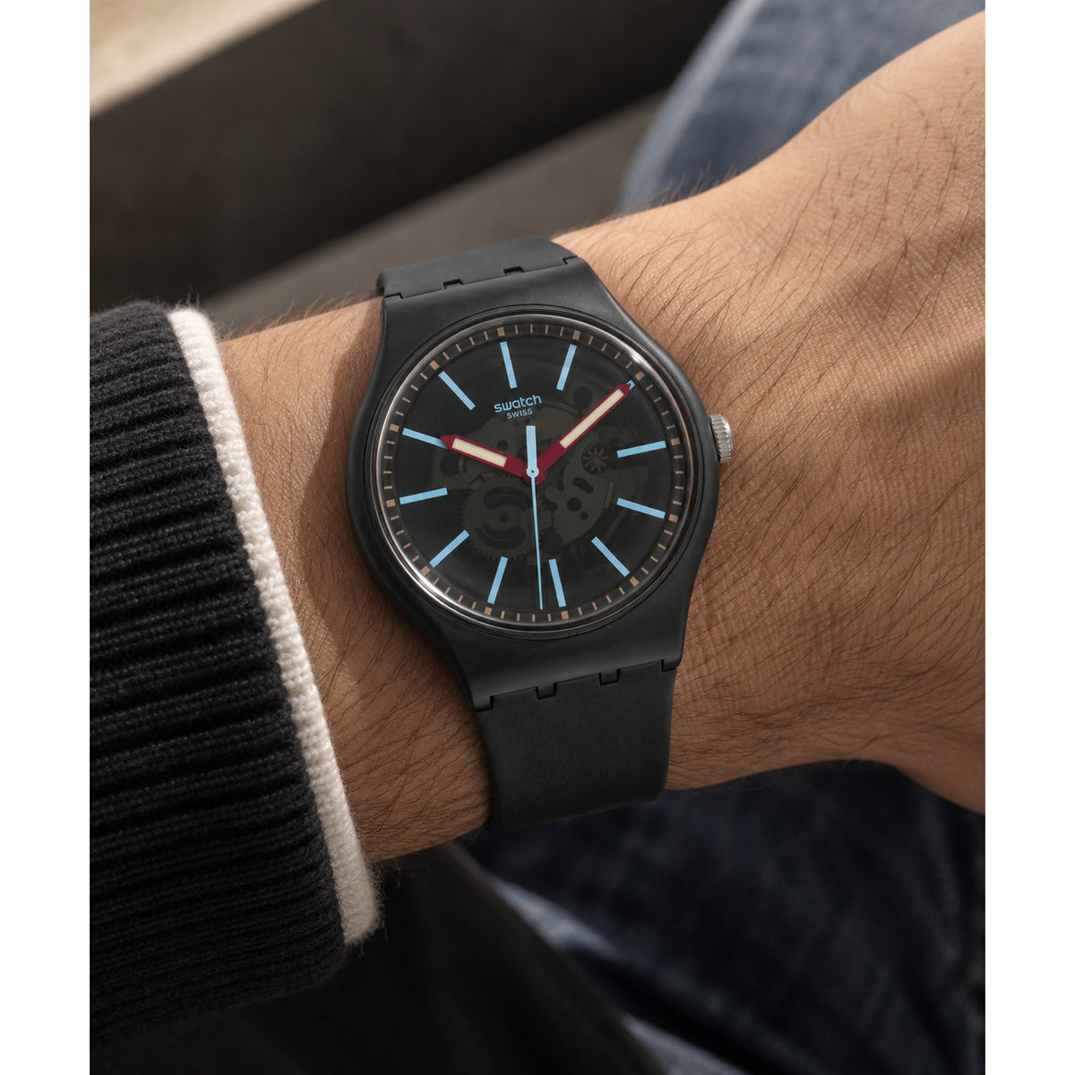 Swatch Cobblestone Street SO29A101 worn on the wrist with gray patterned dial, light blue hour markers, red hands, dark gray case, and matching dark gray strap.
