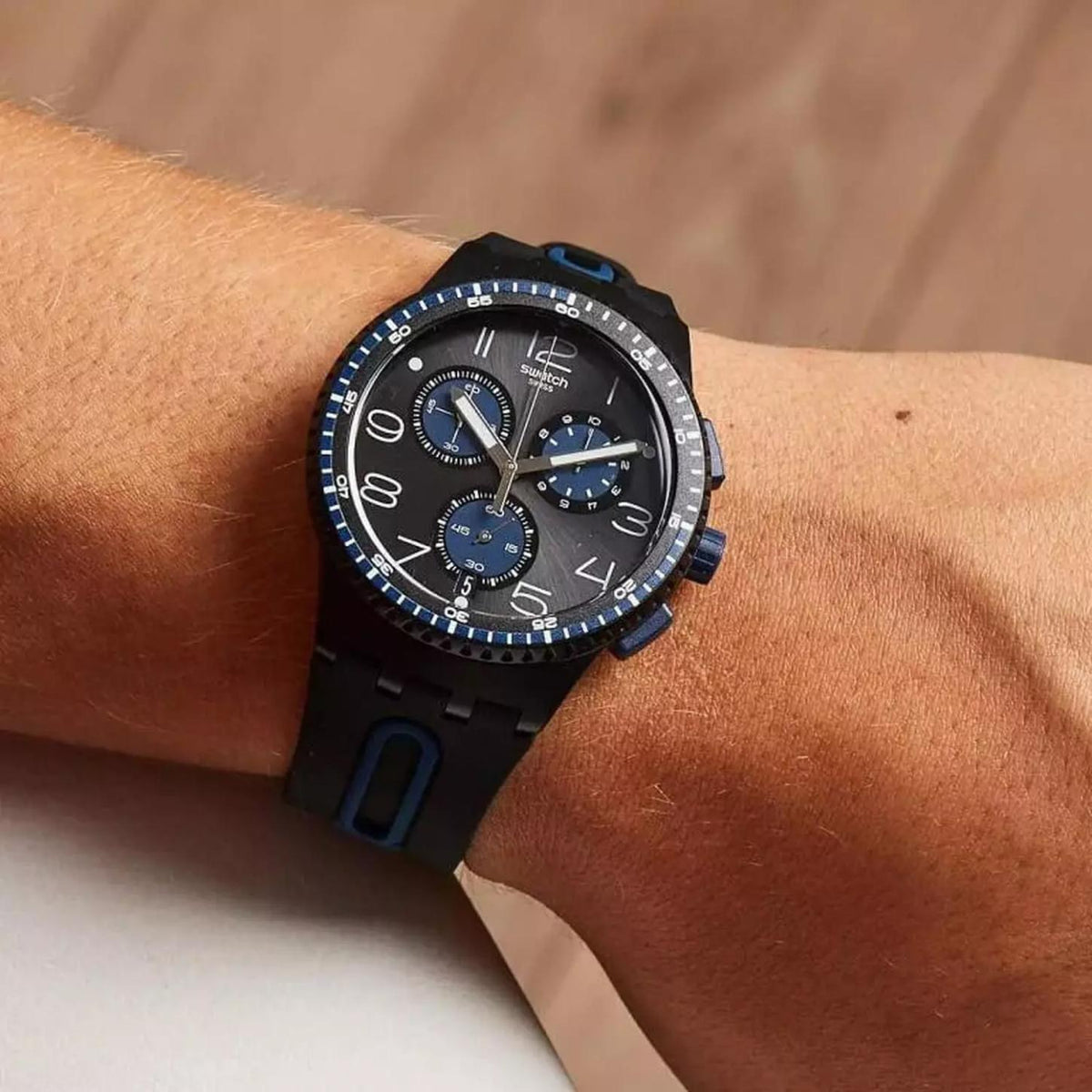 Swatch Kaicco SUSB406 chronograph watch with an anthracite dial, blue subdials and accents, black case, and black strap worn on the wrist.