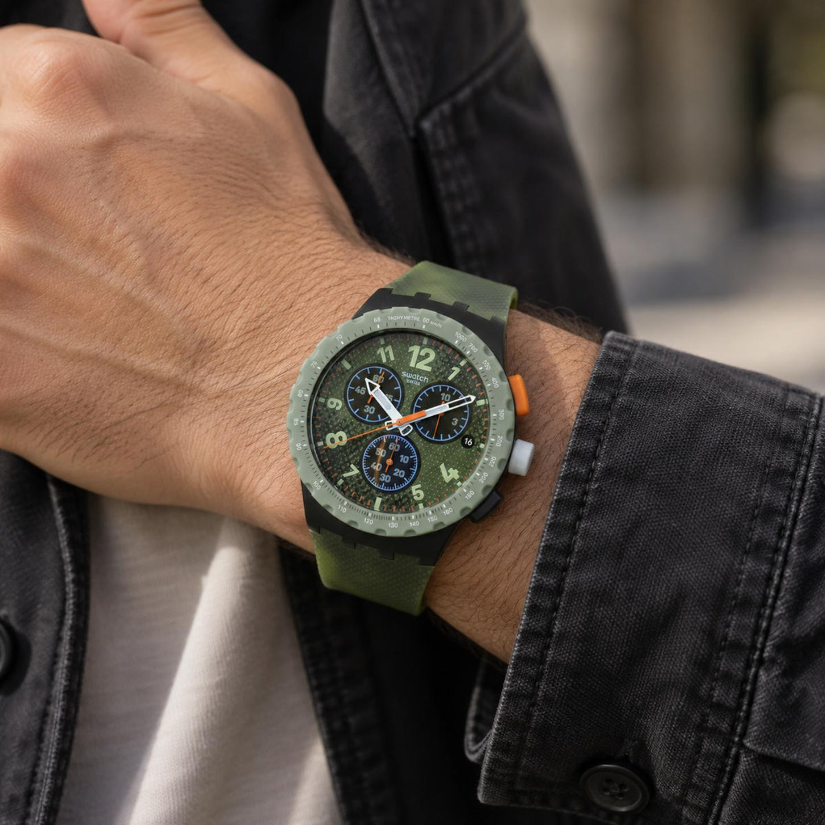 Swatch Midday Camo SUSB423 worn on the wrist with green camouflage chronograph dial, three subdials, orange accents, green tachymeter bezel, and matching green strap.