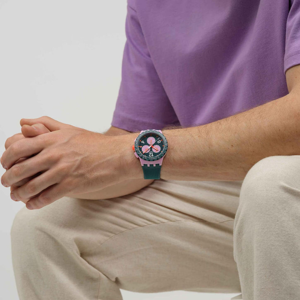 Swatch Moment of Rose SUSP400 worn on the wrist with green chronograph dial, pink subdials and case accents, orange hands, dark green bezel, and matching textured green strap.