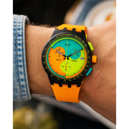 Swatch Neon Signal Flag SUS B422 chronograph watch with a multicolor dial, black case, colorful pushers, and bright orange strap worn on the wrist.