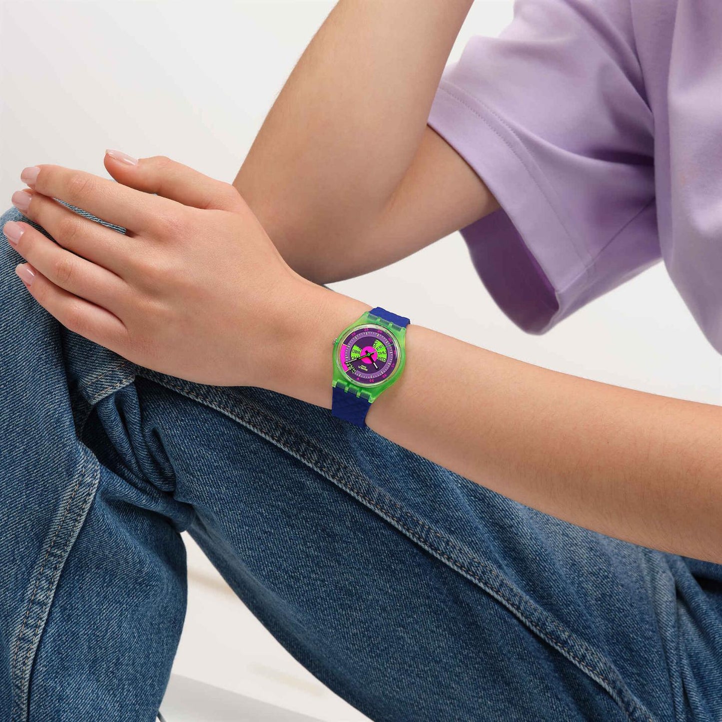 Swatch Neon Skychart SO28G704 watch with a purple dial, translucent green case, colorful day display, and blue strap worn on the wrist.