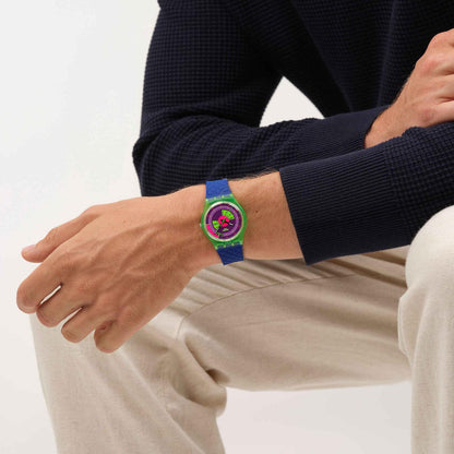 Swatch Neon Skychart SO28G704 watch with a purple dial, translucent green case, and textured blue strap worn on the wrist.