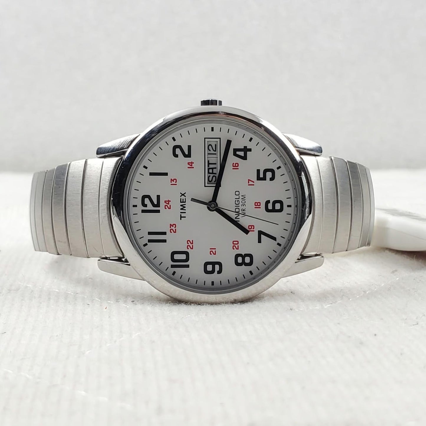Timex Easy Reader Day Date T20461 men’s watch with white dial, red 24-hour markers, and stainless steel expansion bracelet displayed on a flat surface.