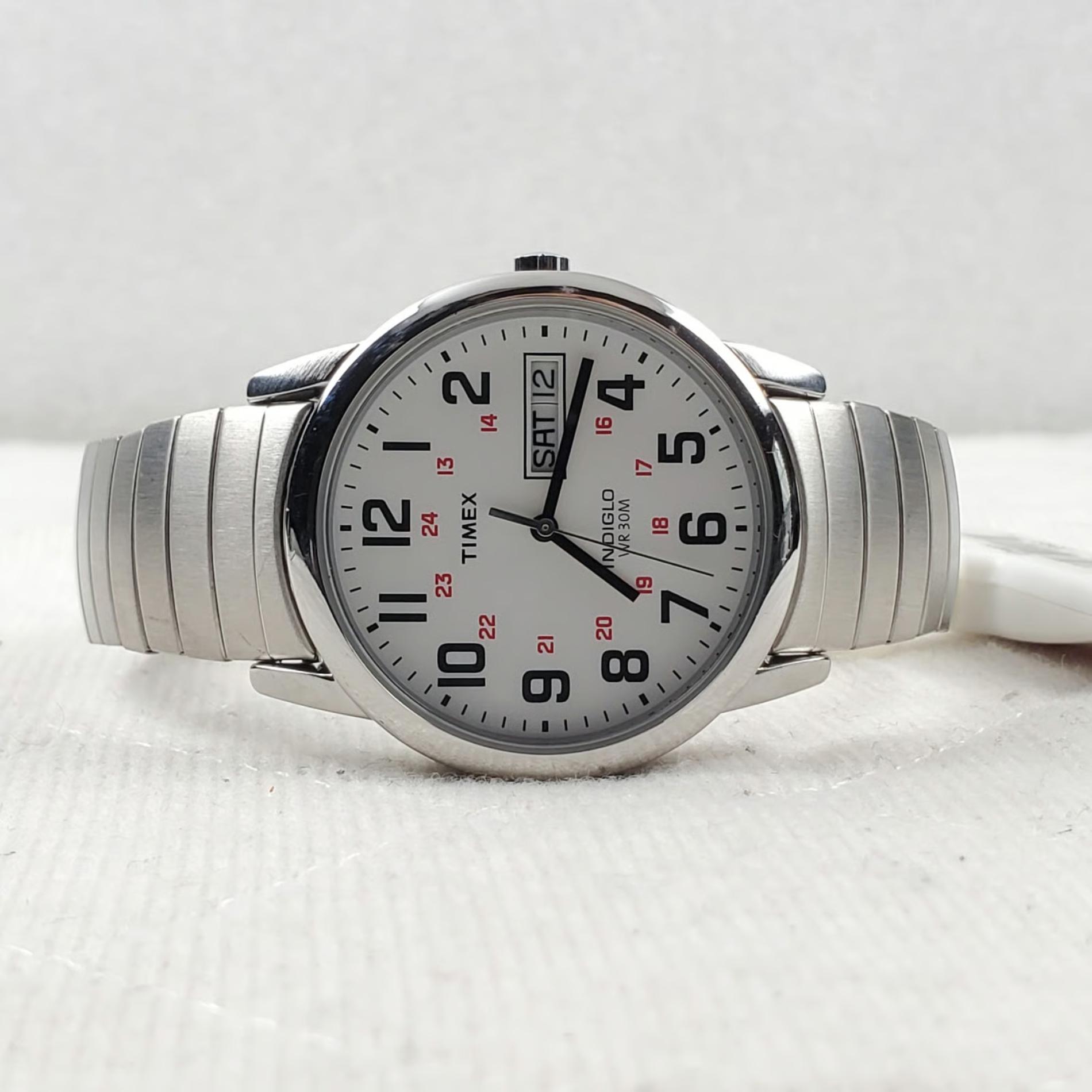 Timex Easy Reader Day Date T20461 men’s watch with white dial, red 24-hour markers, and stainless steel expansion bracelet displayed on a flat surface.