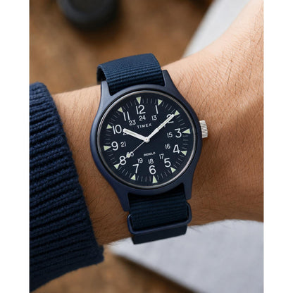Timex MK1 TW2R37300 worn on the wrist with a blue dial, white Arabic numerals, luminous hour markers, blue aluminum case, and matching fabric strap.