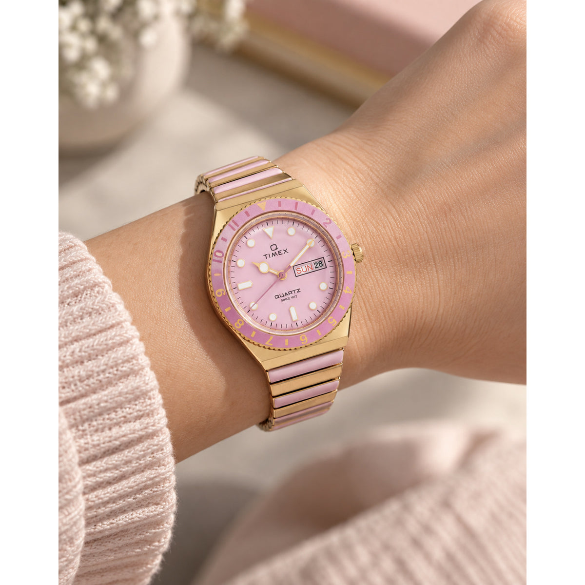 Timex Q Timex TW2W87600VQ with a pink dial, pink bezel, day-date window, and gold-tone bracelet with pink center links worn on the wrist.