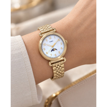 Timex Trend TW2T89500VQ with a mother-of-pearl dial, gold-tone Arabic numeral hour markers, moonphase display, gold-tone case, and matching bracelet worn on the wrist.