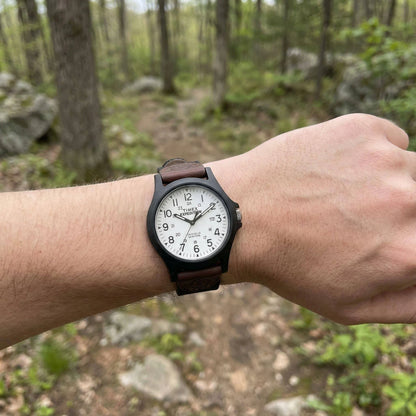 Timex TW4B08200 field watch worn on the wrist with white dial, black case and brown leather and fabric strap.