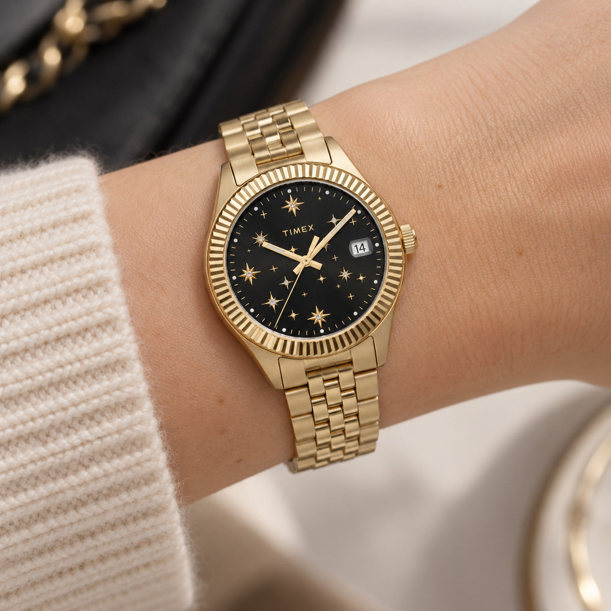Timex Waterbury Celestial Legacy TW2W21700 worn on the wrist with black celestial dial, gold-tone star markers and hands, fluted bezel, date window, and matching gold-tone bracelet.