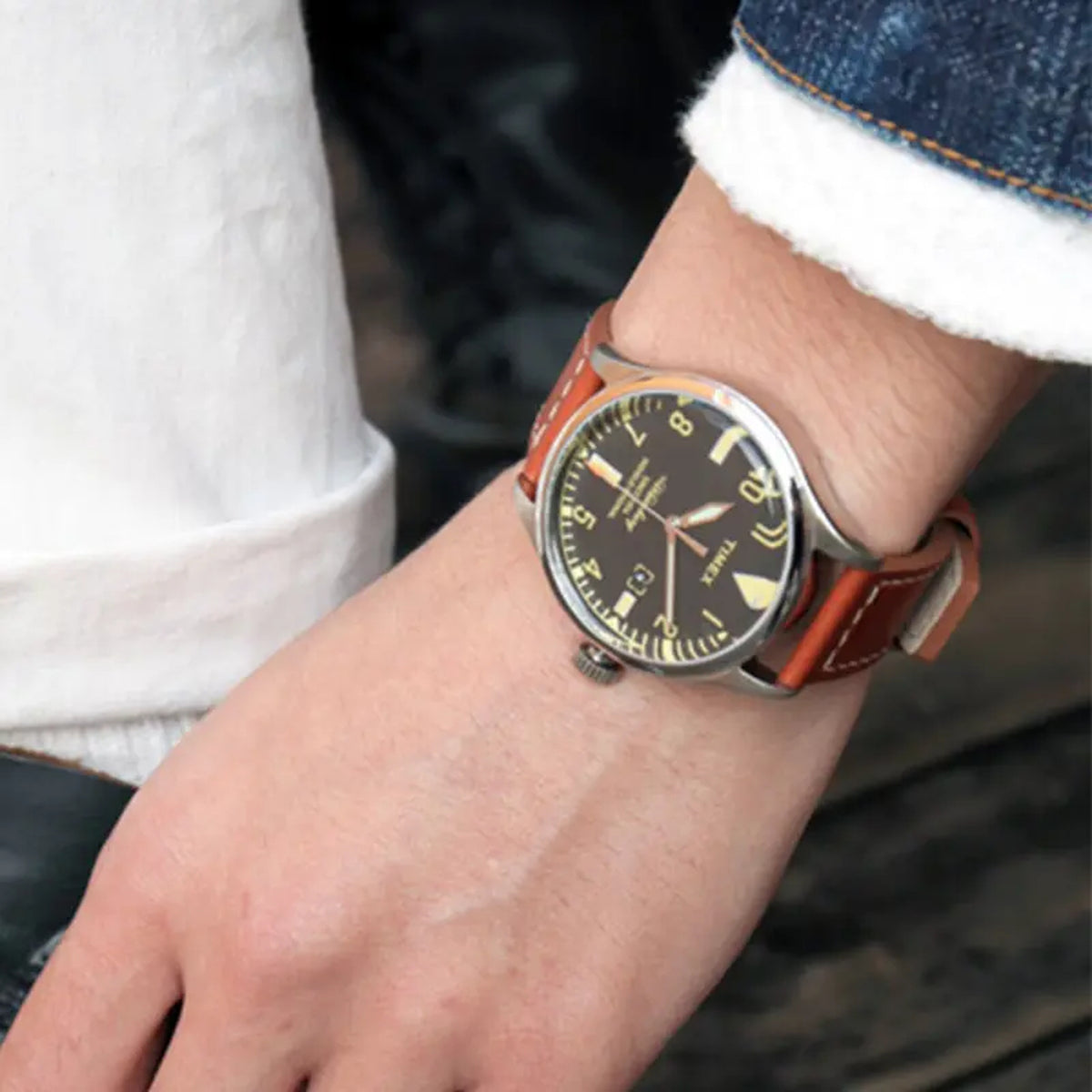 Timex Waterbury TW2P84000 worn on the wrist with black dial, cream-tone numerals and markers, silver-tone case, date window, and brown leather strap with contrast stitching.