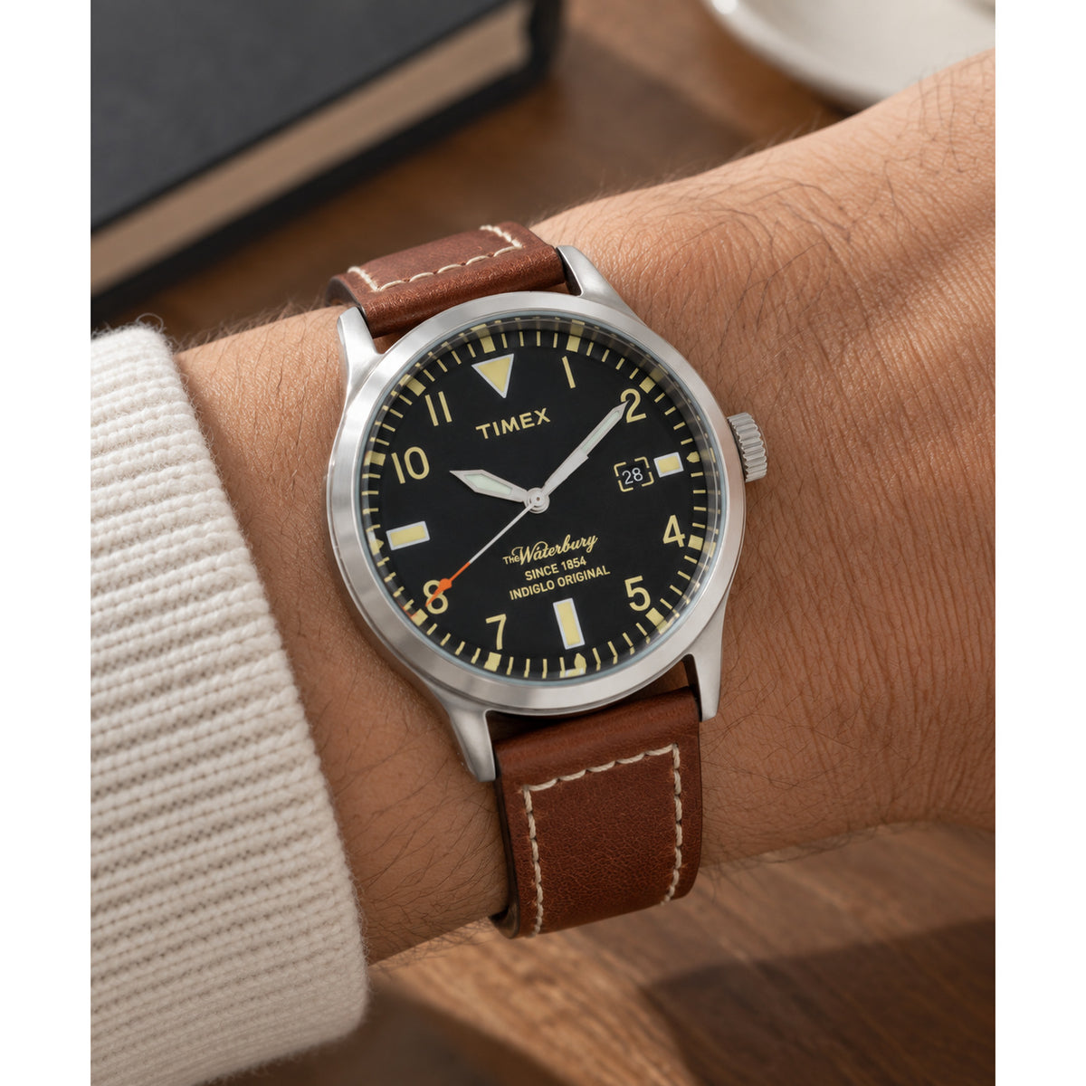 Timex Waterbury TW2P84000 with black dial, cream-tone hour markers and numerals, silver-tone case, date window, orange seconds hand, and brown leather strap with contrast stitching.