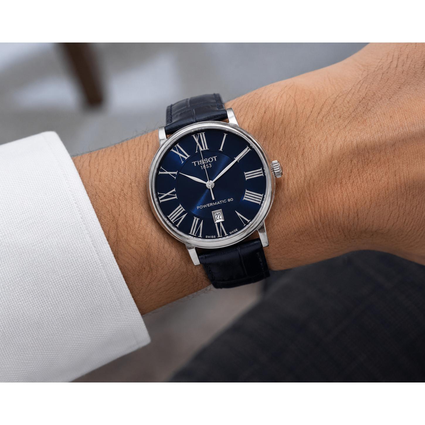 Man wearing the Tissot Carson Premium Powermatic 80 T122.407.16.043.00 automatic dress watch with a blue sunray dial, Roman numeral hour markers, stainless steel case, and blue leather strap in an elegant everyday setting.