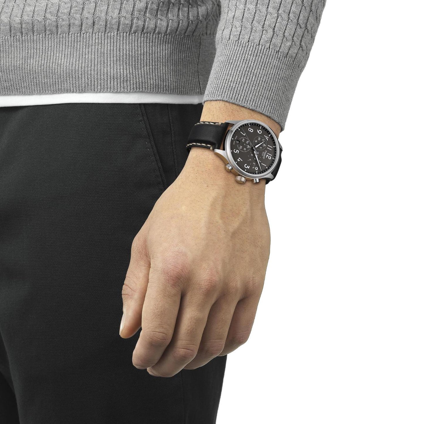 Brazo masculino relajado con jersey gris y pantalón oscuro, llevando en la muñeca el Tissot Chrono XL T116.617.16.062.00 con caja de acero grande y correa de cuero negro.